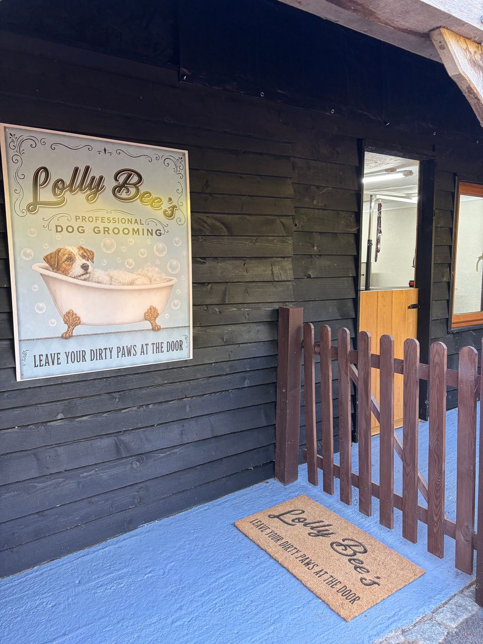 The outside of the lodge: the Lolly Bee's sign, the stable door and a doormat reading "Leave your dirty paws at the door"